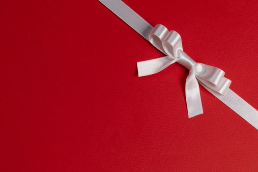White satin ribbon bow on red paper background