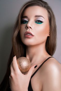 The portrait of model with long hair and perfect skin on a gray background. christmas ball in hand