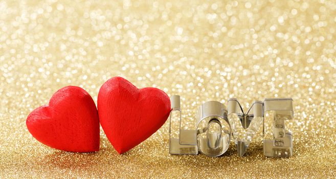 Two red handmade wooden hearts and word love on golden bright glitter lights bokeh background