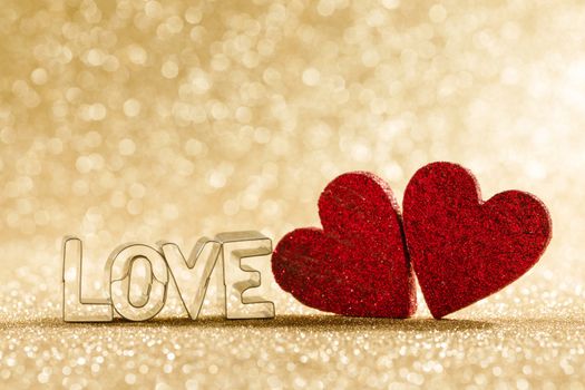 Two red handmade glitter hearts and word love on golden bright glitter lights bokeh background