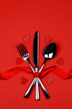 Cutlery set tied with silk ribbon and hearts on red background Valentine day dinner concept