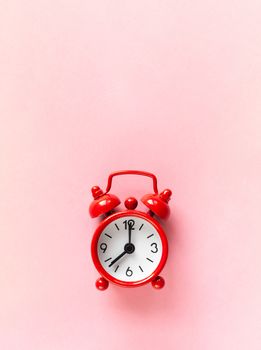 Red small alarm clock on pastel pink background with copy space, flat lay, macro. Minimalism style. Time management, countdown concept. Vertical orientation.
