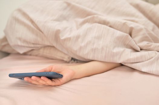 Young Woman With Smartphone Lying In Bed Under The Blanket