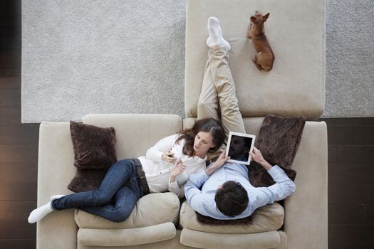 Couple using digital tablet at home sitting on sofa, top view