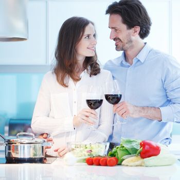 Portrait of a couple having a glass of red wine while cooking dinner