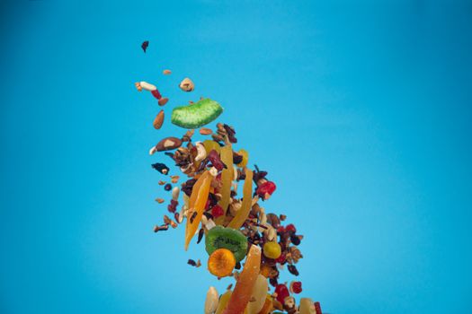 Dried and candied fruits and nuts flying on blue background. Stock photo of healty and nutrient food. Conceptual photo of vegan and vegetarian healty food.