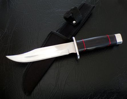 Hunting knife on a black leather background. Bowie knife with scabbard close-up. A handmade knife.