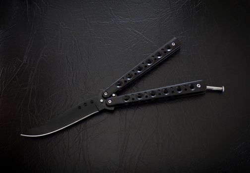 Butterfly knife on a black leather background. Balisong knife.