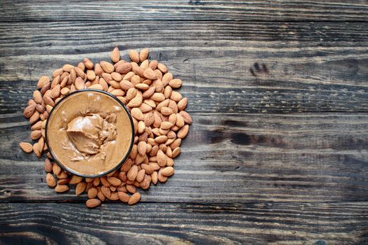 Whole fresh almonds with a bowl of freshly ground creamy almond butter over a rustic table or background.