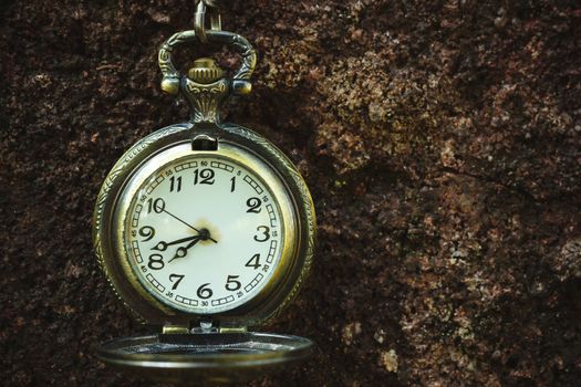 Vintage old pocket watch hanged on the rock background. At 8 o'clock. Closeup and copy space.