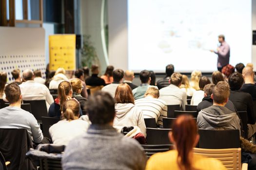 Speaker giving a talk in conference hall at business event. Audience at the conference hall. Business and Entrepreneurship concept. Focus on unrecognizable people in audience.