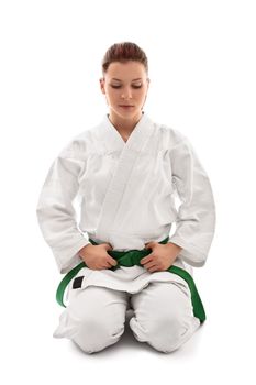 Beautiful female martial arts fighter in a white kimono with green belt in the seiza position looking down, isolated on white background. Calm young girl in a kimono meditating.