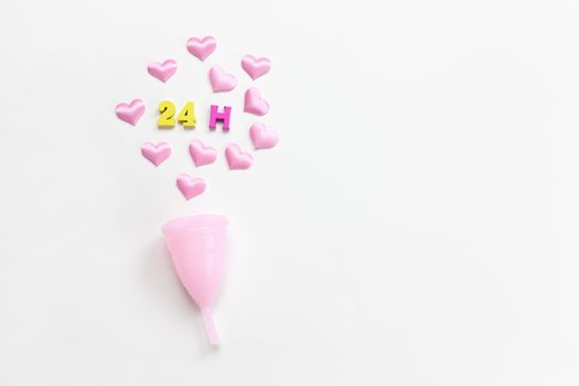 Pink menstrual cup on white background with hearts and designation of use time, 24 hours, laid out in colored numbers and letter. Concept zero waste, savings. Flat lay, copy space. Horizontal.