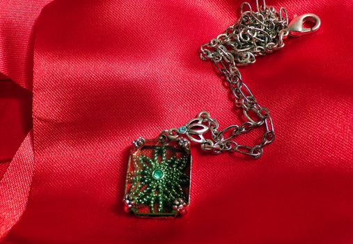 Jewelry pendant made of precious stone with a chain on a background of red silk fabric.