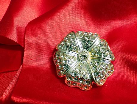 A flower brooch made of metal and precious stones on a red silk fabric.