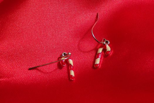 Earrings in the form of caramel sticks on a background of red fabric. Cute children's earrings.