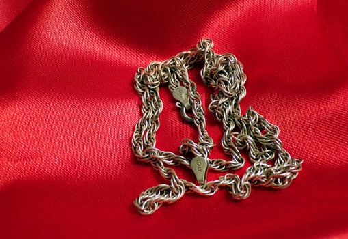 Silver chain close-up. Jewelry made of silver. A thick chain of precious metal on a red silk cloth.