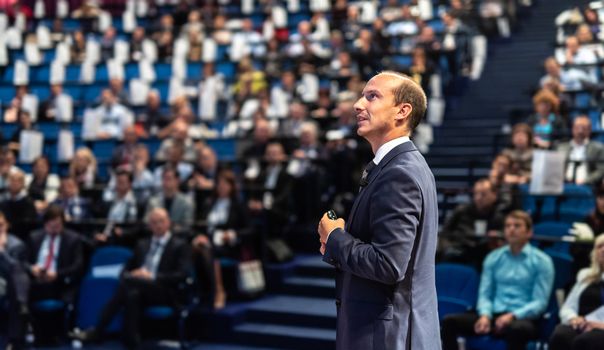 Speaker giving a talk on corporate business conference. Unrecognizable people in audience at conference hall. Business and Entrepreneurship event.