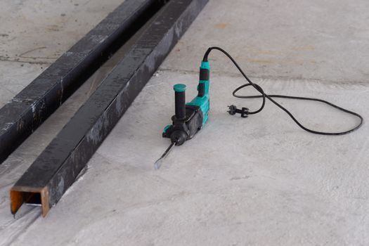 Perforator lies on a concrete floor. Square huge pipes on construction site. Working tool photo.