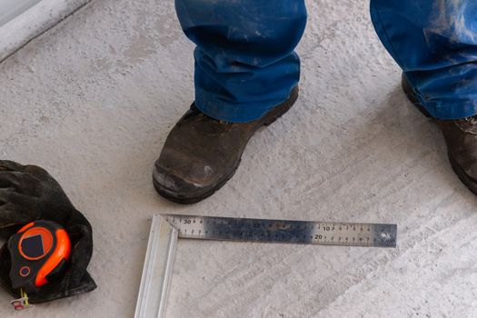 A man is standing on a concrete floor unfinished construction near ruler, measuring tape and metal setsquare.