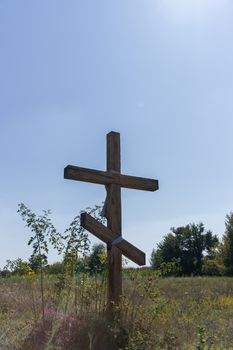 A wooden cross in the middle of the field. Christian symbol.