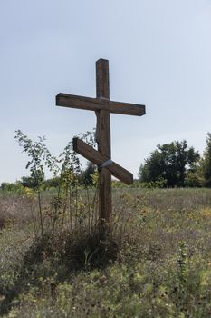 A wooden cross in the middle of the field. Christian symbol.