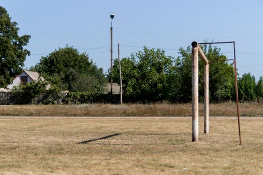 The empty football field with soccer goal in village. The grass is old and yellow.