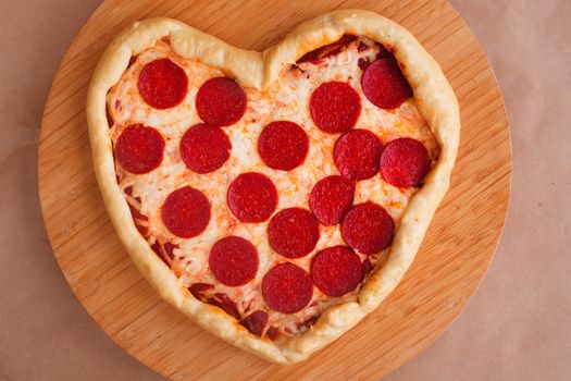 Pizza heart shaped with pepperoni on wooden background. Concept of romantic love for Valentines Day . Love food