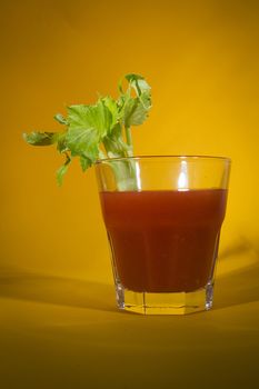 Bloody Mary cocktail with a branch of celery on a yellow background