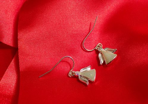 Beautiful angel earrings on red silk fabric. Cute jewelry in the form of angels.