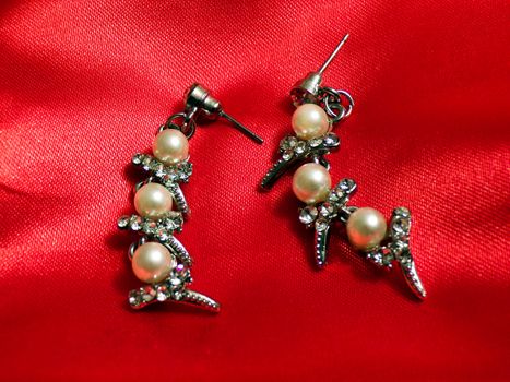 Long earrings made of silver and pearls close-up on a background of red silk fabric. Jeweller ornament.