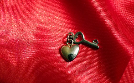Romantic love background for Valentine's day. Heart and key made of metal on a red silk fabric.
