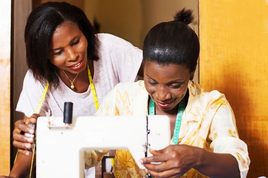 The professional seamstress sews and his trainee assists from behind.