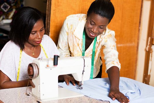 seamstress teaches her  students how to put a shirt under the needle of a sewing machine.