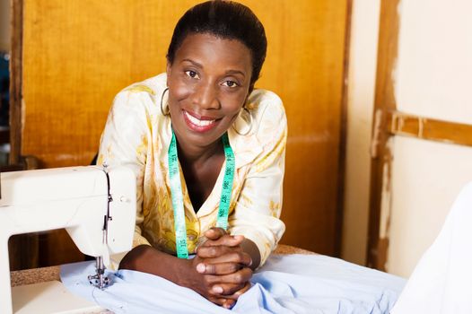 Beautiful woman seamstress smiling leaning on the table of her sewing machine and looking at the camera