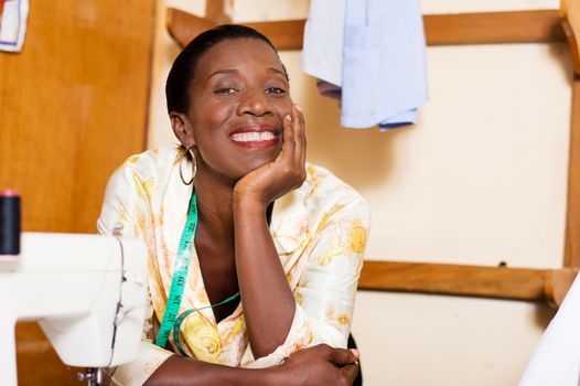 Beautiful woman seamstress smiling leaning on the table of her sewing machine
and hand under the chin
