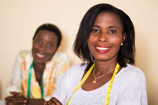 Smiling seamstress in her workshop looks at the camera with her colleague in the background.