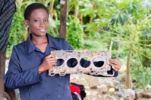 Young woman mechanic holds a damaged car part in her workshop.