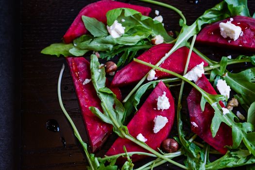 Fresh salad from beetroot, cheese and rocket salad on black wood background