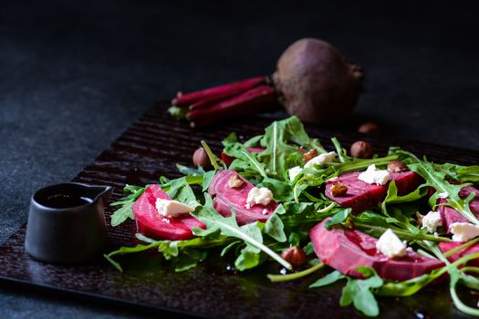 Fresh salad from beetroot, cheese and rocket salad on black wood background