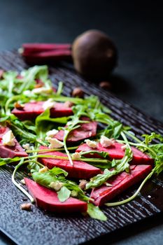 Fresh salad from beetroot, cheese and rocket salad on black wood background