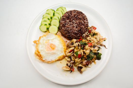 Spicy stir fried squid with basil leaves and chili, Sunny side up egg, served with brown rice. It is famous Thai food. You can change material designed and try to cook for your family.