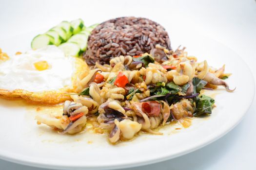 Spicy stir fried squid with basil leaves and chili, Sunny side up egg, served with brown rice. It is famous Thai food. You can change material designed and try to cook for your family.