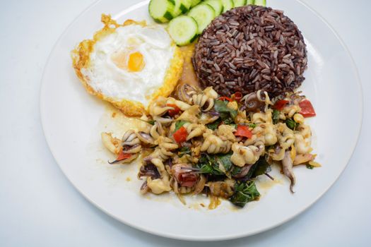 Spicy stir fried squid with basil leaves and chili, Sunny side up egg, served with brown rice. It is famous Thai food. You can change material designed and try to cook for your family.