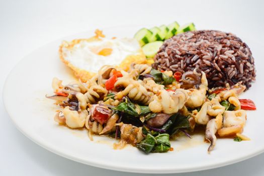 Spicy stir fried squid with basil leaves and chili, Sunny side up egg, served with brown rice. It is famous Thai food. You can change material designed and try to cook for your family.