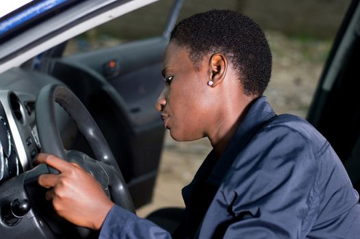 A young mechanic sitting at the wheel of a car, checks her ignition.