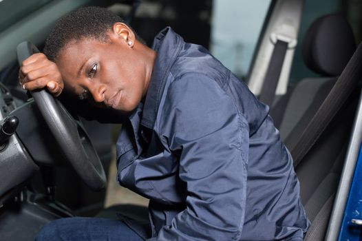 Young woman mechanic sitting at the wheel of a car, head on the wheel and pensive.