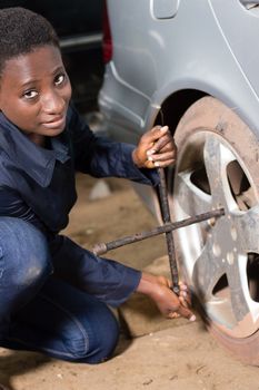 Young woman mechanic on her knee, removes the tire from a car she wants to replace.