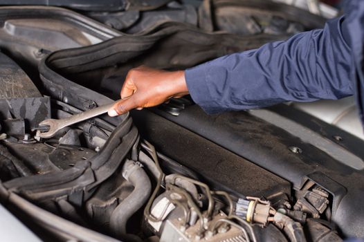 Close-up of a hand holding a key on the engine of a broken car.