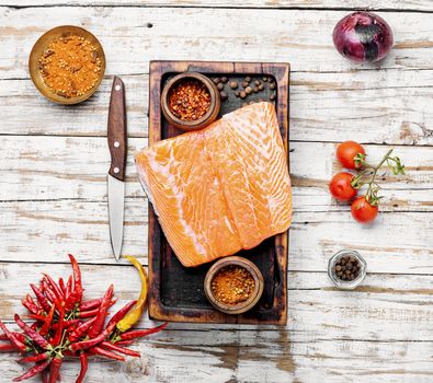 Raw salmon fillet with rosemary on wooden cutting board